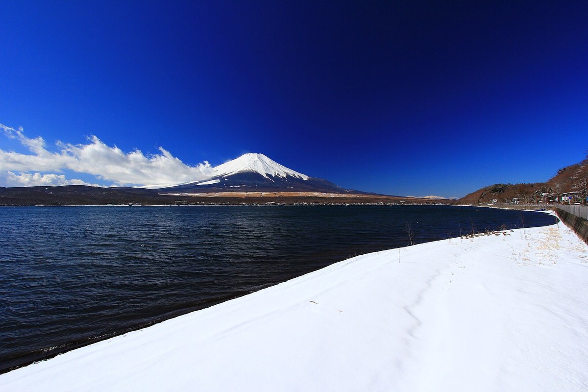 2 月的山中湖北岸：湖邊沙灘整片被白雪蓋住，雪面延伸到水邊，湖對岸是雪頂富士山，天空深藍