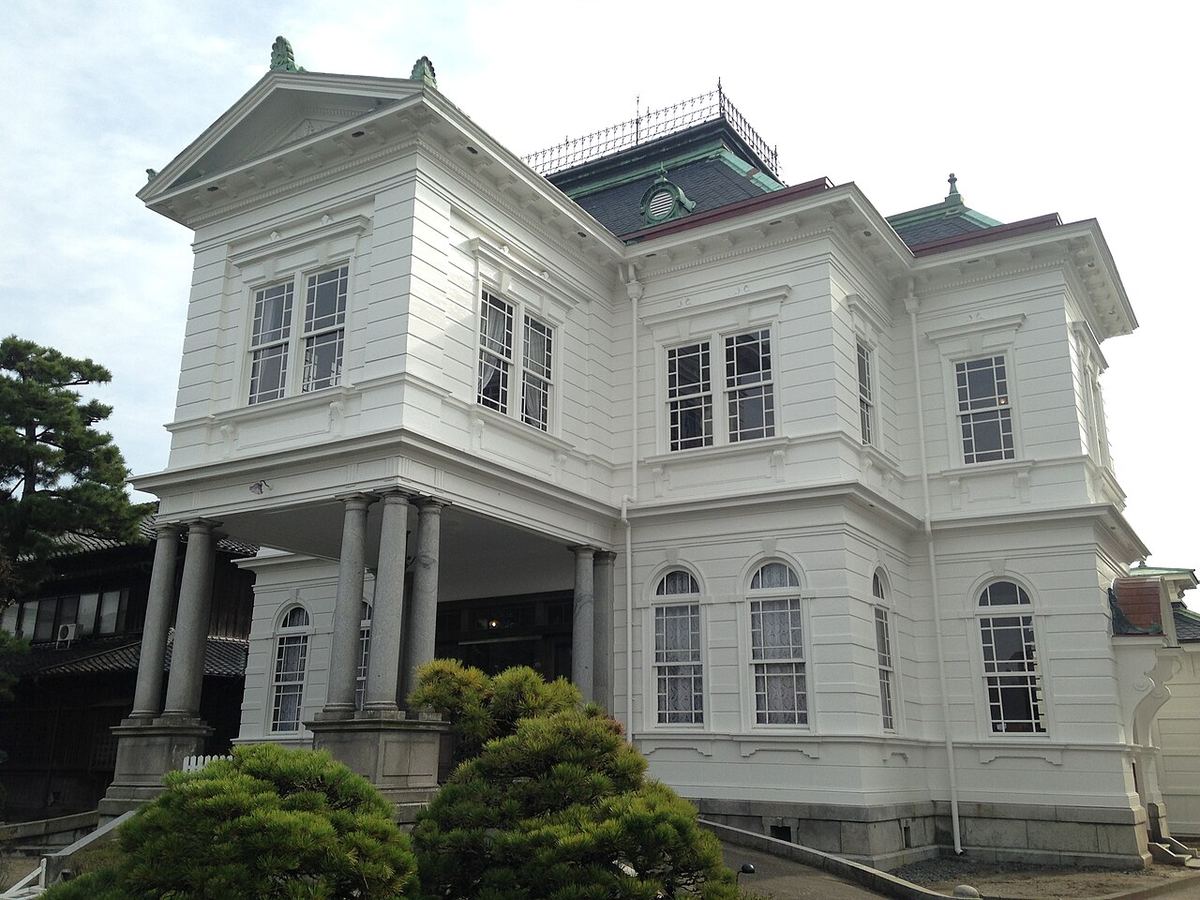 御花的西洋館外觀:兩層樓的白色木造洋樓,三角山牆、綠色銅板屋頂與屋頂鐵欄杆,正面玄關由成組的灰色石柱撐起,前方是修剪成圓形的松樹