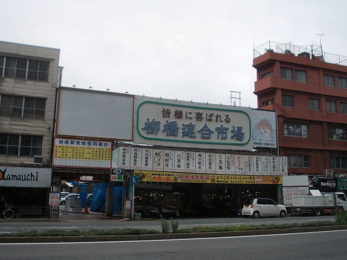 柳橋連合市場臨大馬路的正面:白底藍字「柳橋連合市場」大招牌,下方一整排各店店名的直式看板,入口在看板底下;畫面左邊立著寫「P 24h」的停車場標示
