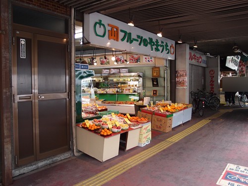 頂棚下的水果店「フルーツのやまうち」,店門口台子上擺滿一盒盒橘子、蘋果等水果,隔壁一家店拉下了鐵捲門