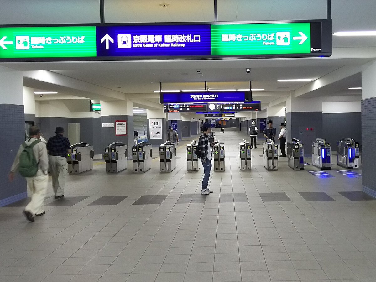 淀站站內一排自動剪票機,上方藍色大招牌寫著「京阪電車 臨時改札口 Extra Gates of Keihan Railway」,兩側綠色招牌是「臨時きっぷうりば」,旅客臉部已由上傳者打上馬賽克