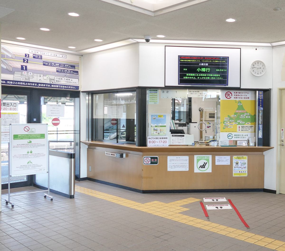 JR 余市站站內:左邊立牌畫著禁止符號與 IC CARD、寫著「当駅ではICカードはご利用出来ません」,旁邊是沒有自動閘門的不鏽鋼改札通道;中間是みどりの窓口,櫃檯貼著「みどりの窓口営業時間 8:00~17:20」,上方螢幕顯示「小樽行」