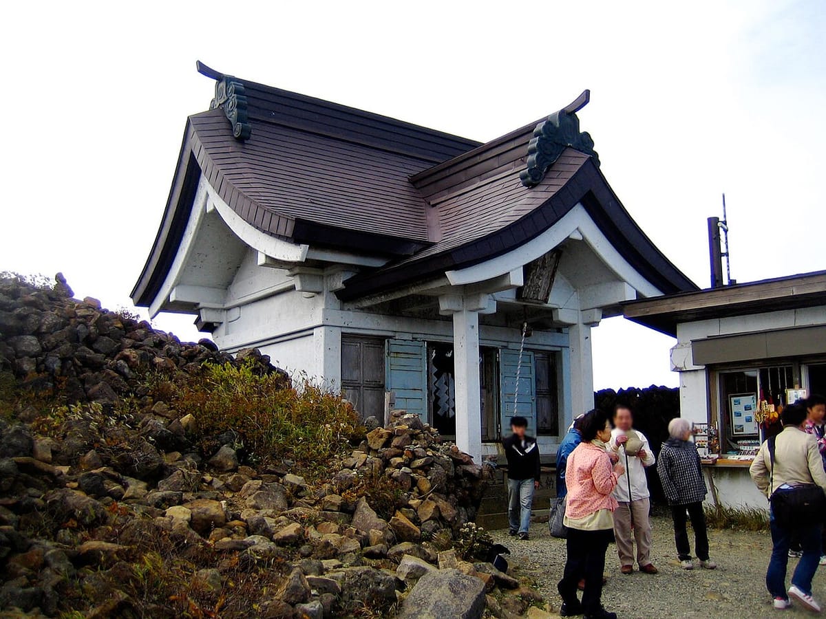 刈田岳山頂的刈田嶺神社奧宮社殿,白牆社殿旁堆著火山岩,參拜者聚在殿前